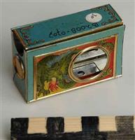 B2008-0707 achterkant.jpg; B2008-0707; Rechthoekige doos met de afbeelding van een vrouw met toorts met diverse openingen en een schuifje met daarin een gaatje; luciferdoosjeshouder